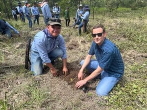 Two men kneeling to plant a pine seedling